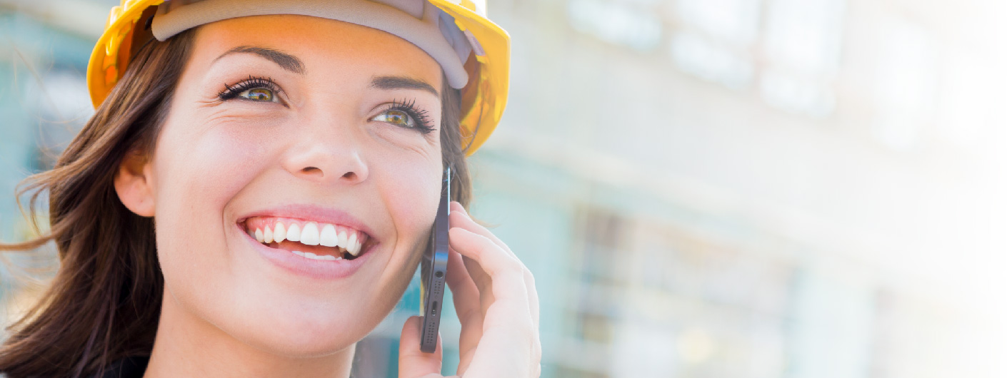 Smiling woman in yellow hardhat talking on a mobile phone