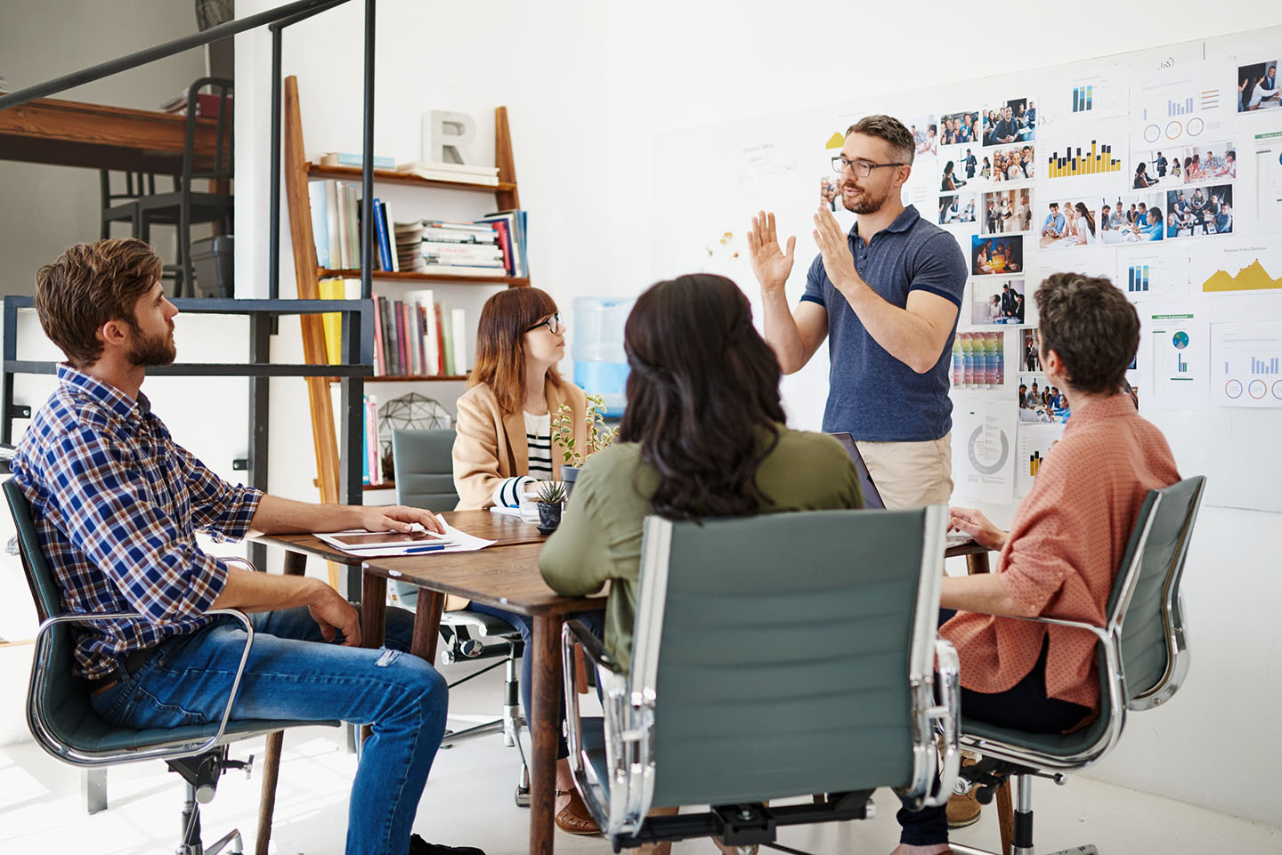 Men and women sitting at a desk listening to a man with glasses speaking