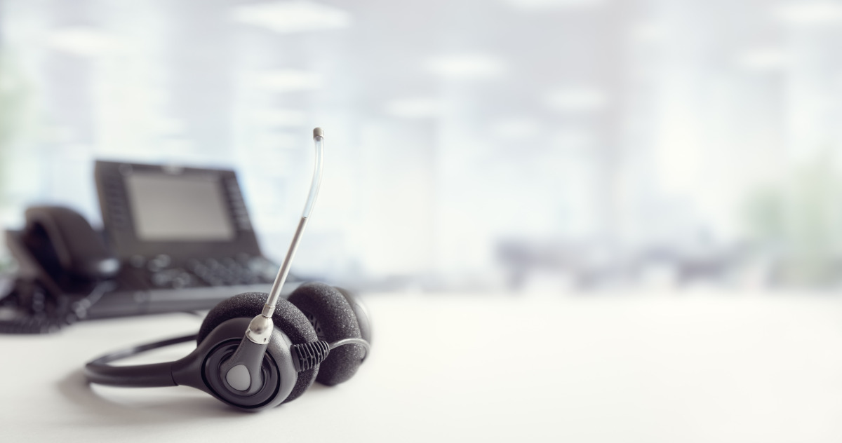 VoIP headphones resing on a white table with a business phone in the background