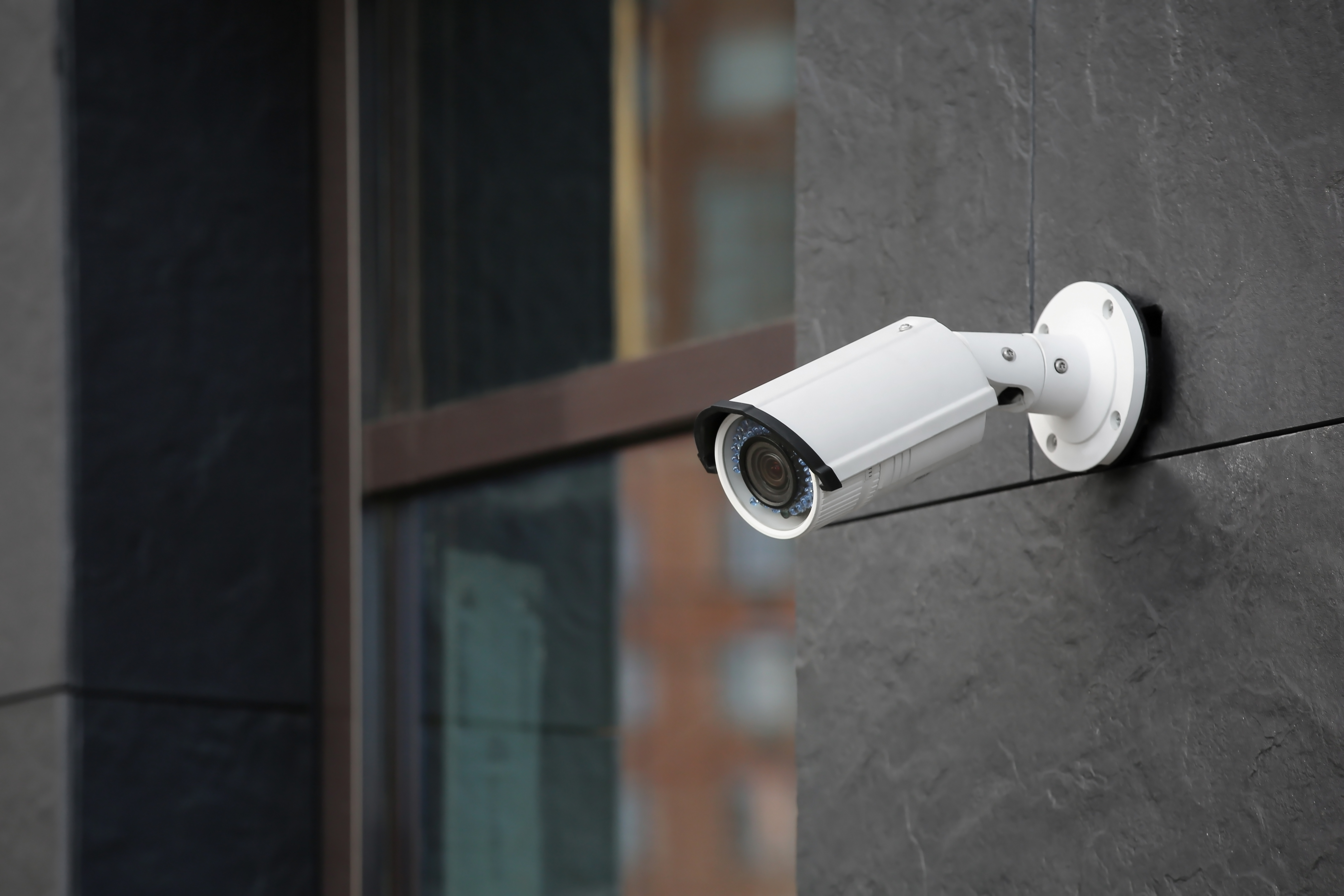 A white surveillance camera mounted on an exterior wall of a business
