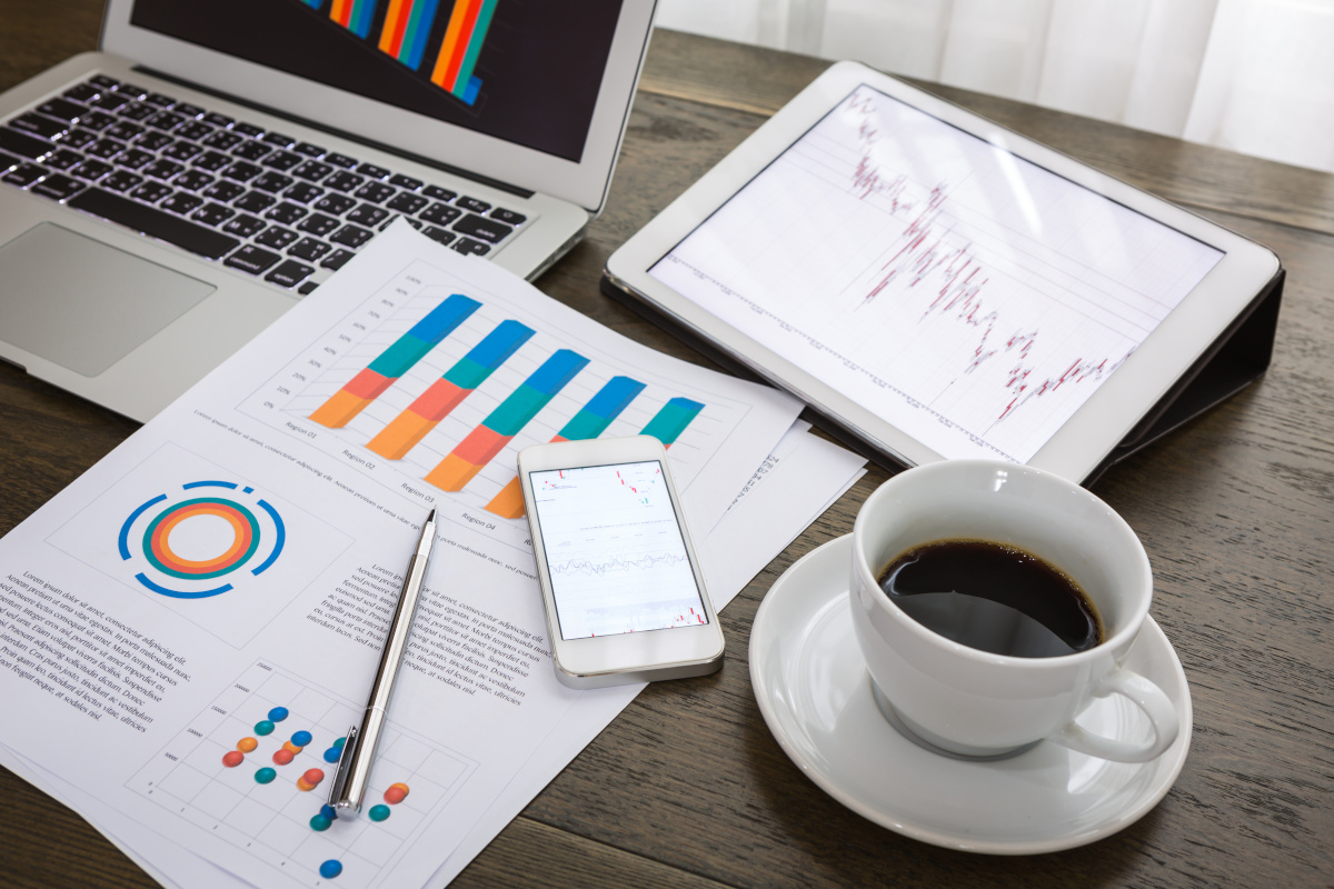 Papers showing graphs, a cup of coffee, and a cell phone on a desk