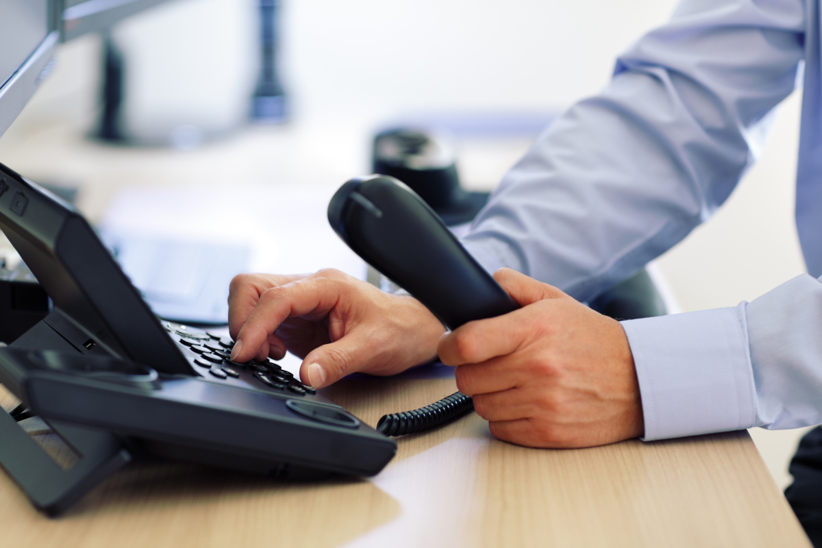 A person dialing an office desk phone