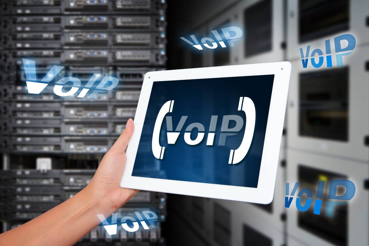 Close up of hands holding tablet with words 'VoIP' on screen with server room in background.