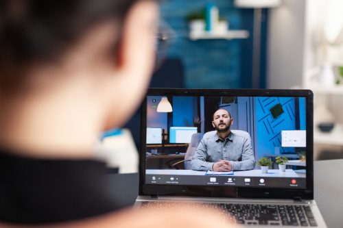 A woman is seated at a desk with a laptop, participating in a video call with a man visible on the screen.